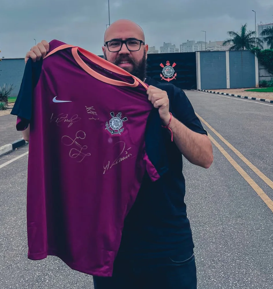 Digão segurando uma camisa autografada em frente à entrada de um centro de treinamento